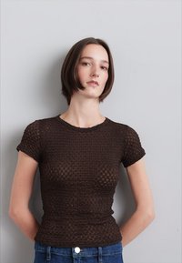 Hnědý pletený top s krátkým rukávem, s texturovaným vzorem, přiléhavý střih a kulatý výstřih, v kombinaci s modrými džínami s vysokým pasem.