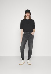 Polo negru cu mâneci scurte, blugi gri tapered și adidași albi. Șapca are detalii cu logo. Design simplu, modern.