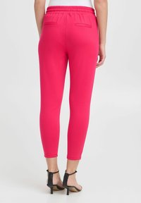 Světle růžové kalhoty vyrobené z elastické tkaniny, s elastickým pasem, slim fit a dvěma zadními kapsami.