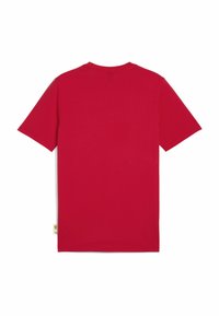 Camiseta de algodón roja con mangas cortas, un escote redondo y la parte de atrás lisa. Presenta una pequeña etiqueta amarilla cerca del dobladillo.