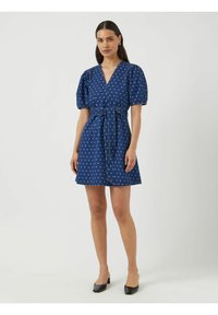 Sininen pilkullinen mekko lyhyillä puffihihnoilla, V-pääntiellä ja vyötäröllä siteellä, valmistettu kevyestä kankaasta.