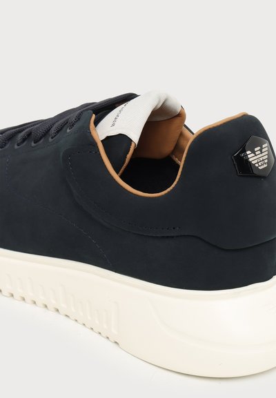 Baskets basses noires avec semelle blanche, doublure intérieure beige et emblème noir du logo sur le talon.