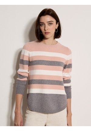 Kobieta z krótkimi brązowymi włosami, nosząca kolczyki koła i sweter z długim rękawem w poziome paski w kolorach różowym, białym i szarym, na jednolitym tle.