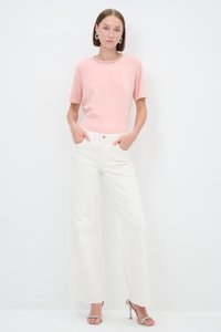 Pink short-sleeve shirt with a decorative neckline, paired with white wide-leg trousers featuring front pockets and a button closure. Silver heels.