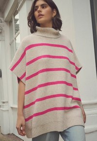Beige strikket sweater med lyserøde vandrette striber, høj hals og korte ærmer, suppleret med lyseblå jeans. Blød tekstur og løs pasform.