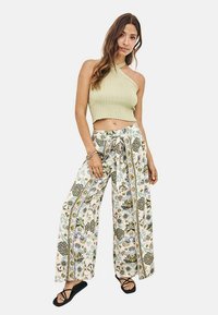 Top corto de canalé verde claro combinado con pantalones de pierna ancha estampados con flores en tonos azules y verdes sobre un fondo crema. Se llevan sandalias negras.