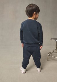 Survêtement pour enfant bleu marine en coton doux, avec des manches longues et des poignets élastiques. Baskets blanches avec des accents rouges.
