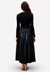 Zwarte ribbelige lange mouwen top, gecombineerd met een zwarte nep leren maxi rok met een elastische tailleband, gezien vanuit de achterkant.