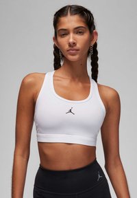 Witte sportbeha van rekbare stof, met een zwart Jordan-logo in het midden en brede banden. Gladde textuur, cropped ontwerp.