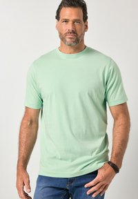 Mintgroen katoenen T-shirt met korte mouwen, ronde hals en zachte textuur, gecombineerd met blauwe spijkerbroek. Subtiele merkaanduiding op de borst.