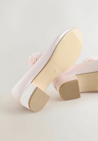 Rózsaszín szatén magas sarkú cipő, lekerekített orral, alacsony blokk sarokkal és virágdíszítéssel a hátoldalán. Texturált gumitalp a jobb tapadás érdekében.