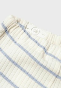 Gros plan sur un tissu léger et texturé avec de fines rayures bleues et une fermeture à bouton, mettant en avant un design décontracté et doux.