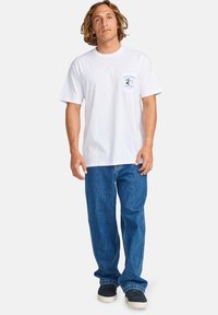 White short-sleeve t-shirt with a chest pocket featuring blue graphic text, paired with relaxed-fit blue jeans and black sneakers.