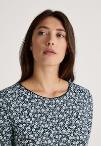 Floral-patterned top in dark green featuring white flowers, a rounded neckline, and a smooth fabric texture.