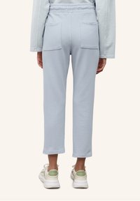 Světle modré, středně vysoké tepláky s elastickým pasem, dvěma zadními kapsami a zkrácenou délkou. V páru s bílými teniskami s zelenými akcenty.