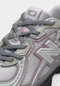 Κοντινό πλάνο γκρι και απαλό ροζ αθλητικού παπουτσιού New Balance με υφή από διχτυωτό υλικό, χοντρές κορδόνια και εξέχον λογότυπο "N" στην πλαϊνή πλευρά.