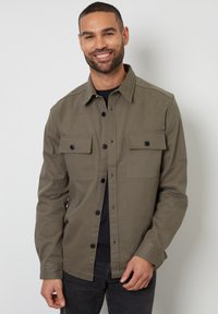Olijfgroene button-up shirt van stevig materiaal, met twee borstzakken met zwarte knopen en een klassieke kraag.