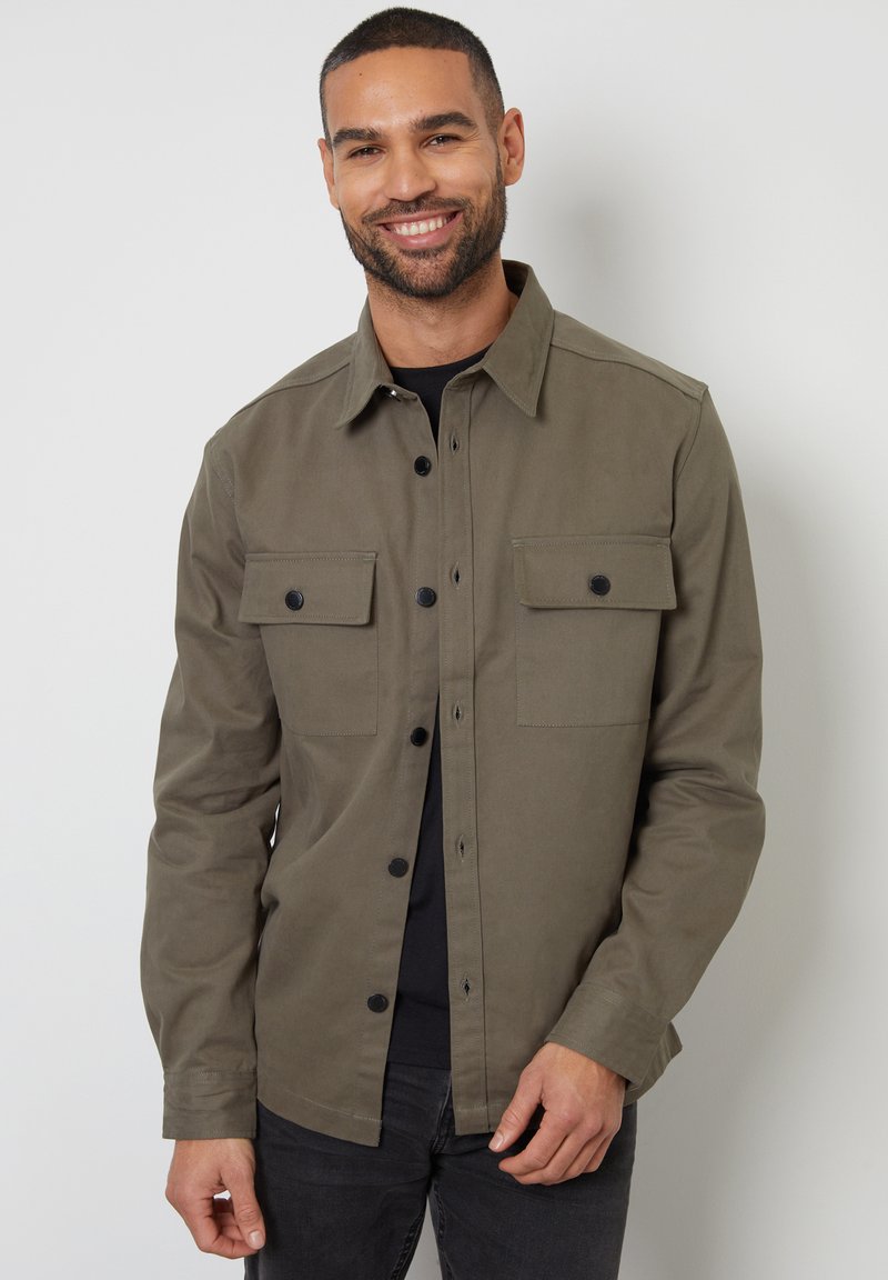 Olijfgroene button-up shirt van stevig materiaal, met twee borstzakken met zwarte knopen en een klassieke kraag.