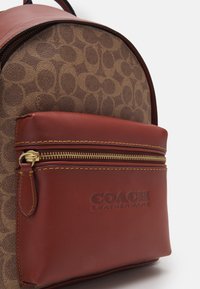 Brązowy plecak skórzany w wzór z bordową skórzaną przednią kieszenią. Posiada złoty zamek i szczegóły z logo. Szyte akcenty w kolorze żółtym.