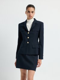 Mörkblå ribbad blazer med guldknappar, utrustad med två framfickor, ihop med en matchande figurnära kjol. Turtleneck underneath.