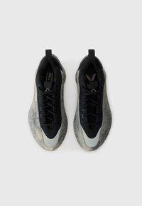 Des chaussures de sport noires avec une semelle intermédiaire grise à motifs. Elles présentent une partie supérieure texturée avec des lacets noirs et un accent gris réfléchissant.
