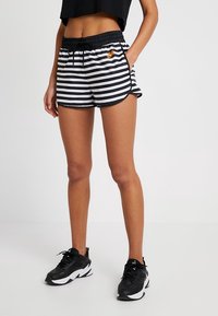 Black and white striped shorts with a drawstring waist, side pockets, and orange Nike logo. Styled with black athletic shoes.