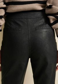 Zwarte leren broek met een gladde textuur, voorzien van twee achterzakken en een aansluitende pasvorm, gecombineerd met een gestreepte trui.