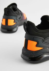 Black and orange sneakers featuring a textured upper, padded collar, and rubber sole with speckled detailing. Striking color accents on the sides.