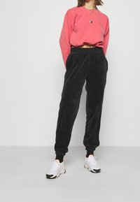 Röd kort sweatshirt med sänkta axlar, ihop med svarta corduroy joggers med resår i midjan och ärmar. Vita sneakers med rosa accenter.