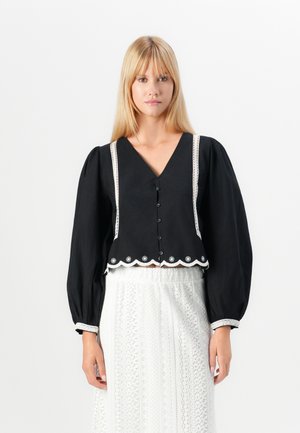 Black cropped blouse with voluminous sleeves, V-neckline, button front, and white lace trim along the neckline and hem, featuring scalloped edges.