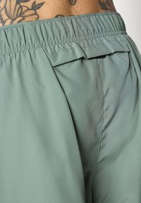 Pantalones de color verde claro, con cinturilla elástica y textura suave, que presentan un diseño de bolsillo trasero doblado y un brillo sutil.