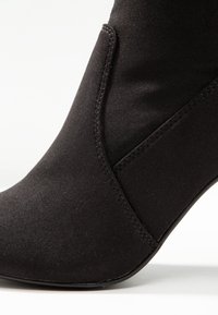 Botín negro de tobillo hecho de tela suave con un diseño ajustado, que presenta una forma curvada y detalles de costura mínimos.