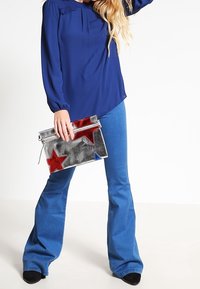 Blusa blu navy a maniche lunghe con dettagli a piastra abbinata a jeans svasati azzurri. Clutch argentata con accenti a stella rossi e blu.