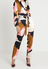 Vzorovaný dvoudílný outfit vyrobený z hladké tkaniny; barvy zahrnují růžovou, černou, hnědou a krémovou. Obsahuje sakou s páskem a tapered kalhoty.