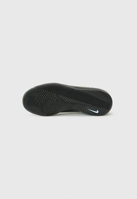 Semelle de chaussure de sport noire avec un motif en caoutchouc texturé, présentant un logo Swoosh blanc et un design de bout incurvé pour une meilleure traction.