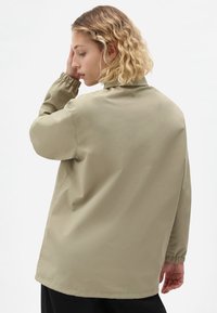 Beige vindjakke med elastiske manchetter, en afslappet pasform og en glat, let tekstur. Bagfra ses et minimalistisk design og en simpel krave.