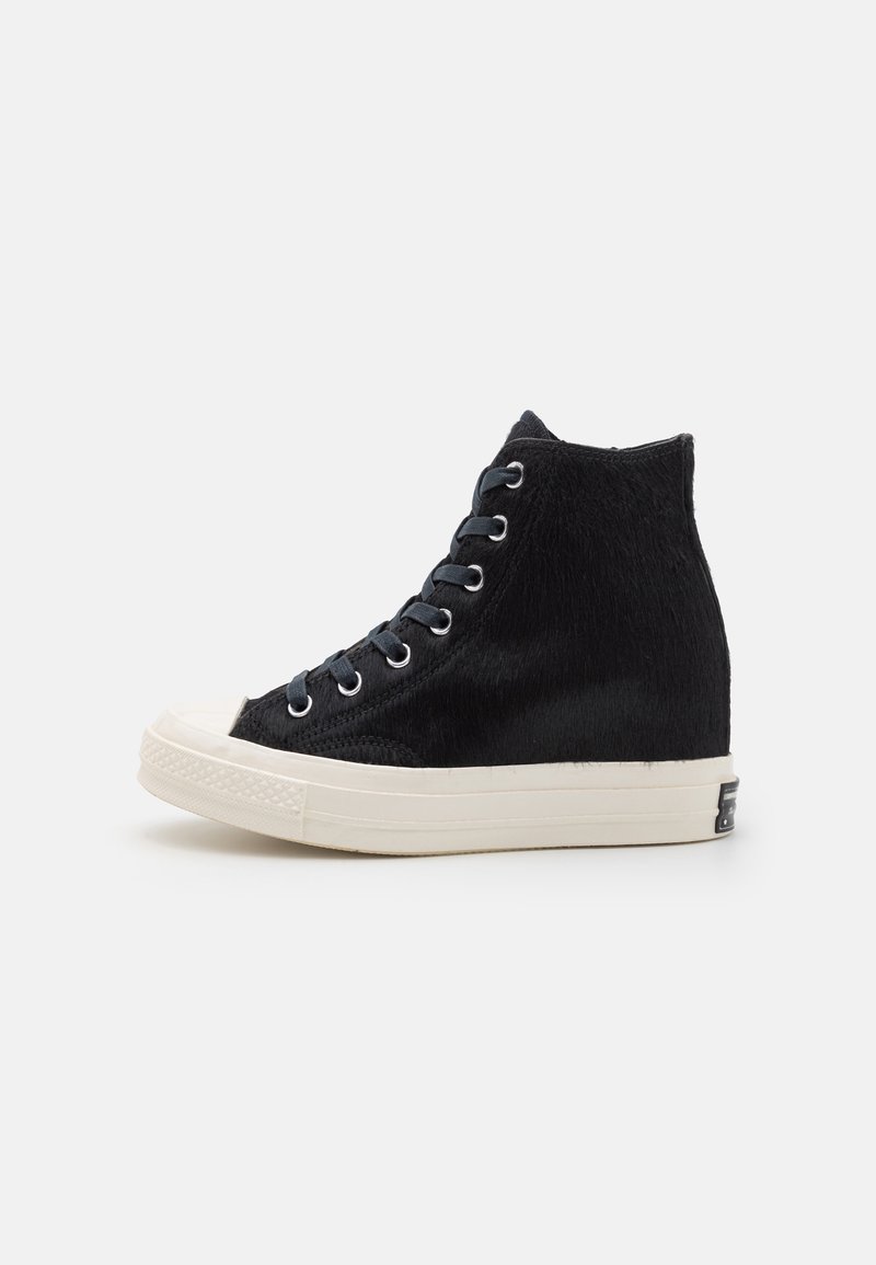 Zapatillas altas negras con parte superior de tela texturizada, suela de goma blanca, puntera redonda y cordones negros a través de ojales plateados.