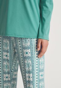 Maglietta turchese a maniche lunghe abbinata a pantaloni blu e bianchi a fantasia con intricati motivi di stelle, foglie e forme geometriche.