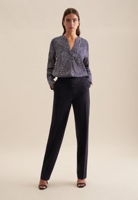 Blusa a pois blu navy con scollatura a V e maniche lunghe, abbinata a pantaloni neri su misura. Entrambi i capi hanno una superficie liscia.