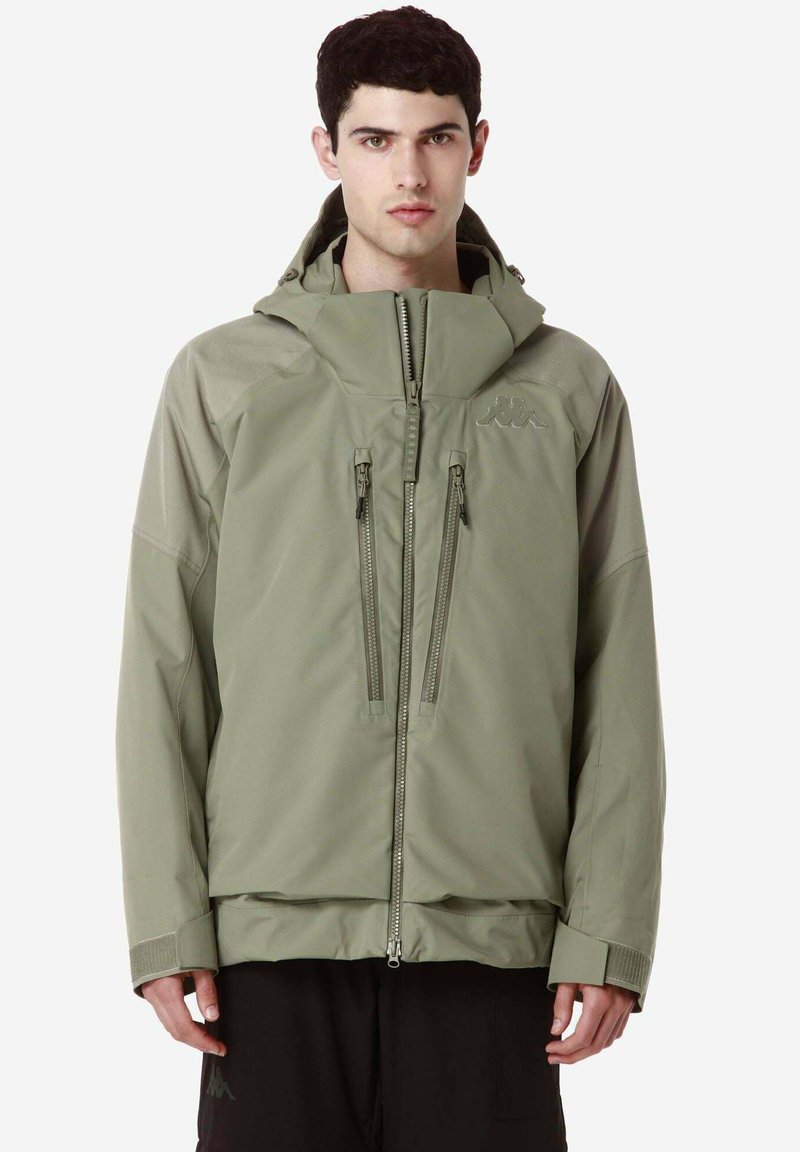 Giacca impermeabile verde oliva con cappuccio, tasche frontali con zip, polsini elastici e una vestibilità leggermente ampia per il massimo comfort.