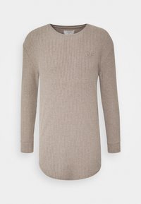 Béžový top s dlouhými rukávy a strukturovaným žebrováním, kulatým výstřihem a malým logem vyšitým na hrudi, s mírně zakřiveným spodním lemem.