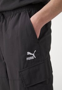 Zwarte cargoshorts met een elastische tailleband, voorzien van een zijzak en een wit Puma-logo op het linkerbovenbeen. Glad, lichtgewicht stof.
