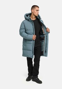 Light blue padded coat with a hood, featuring an open front and orange accents. Worn over a black shirt and paired with black pants and boots.