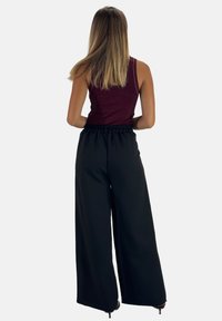 Zwarte wijde broek met een elastische tailleband, gecombineerd met een bordeauxkleurig mouwloos topje, gezien van achteren, waarbij de gladde textuur van de stof wordt getoond.