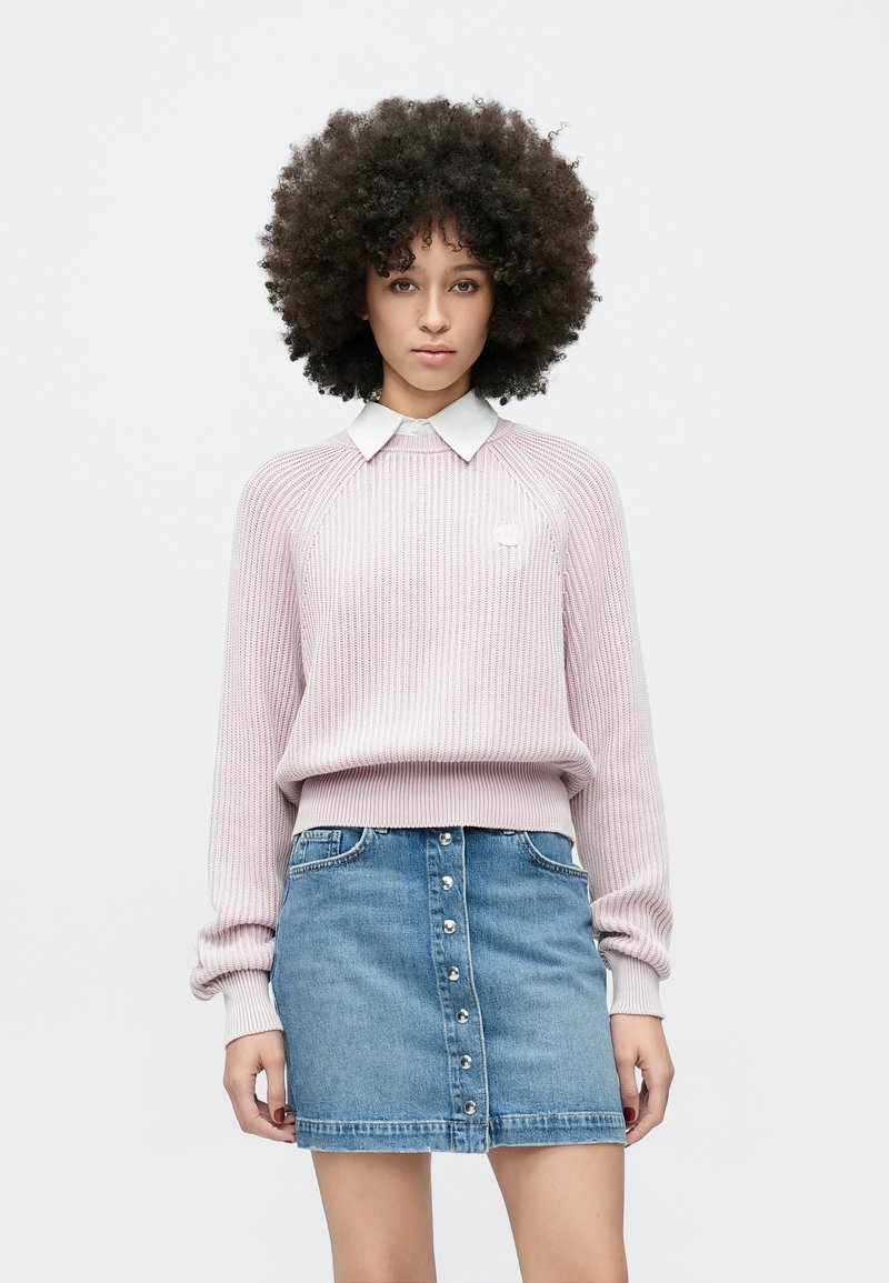 Gaisīgi rozā ribota džemperis ar garām piedurknēm un zem tā balta krekliņa apkakle, kopā ar zilām džinsa miniklātām ar priekšējām pogām.