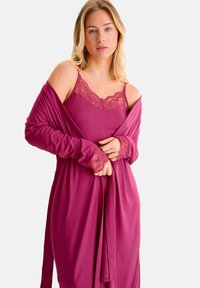 Chemise prune avec bordure en dentelle au niveau de l'encolure et des manches. Tissu doux, design ajusté, devant ouvert avec une taille nouée. Manches longues.