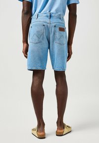 Jasnoniebieskie szorty dżinsowe o luźnym kroju, z dwoma tylnymi kieszeniami, widocznym przeszyciem, skórzaną naszywką z logo oraz postrzępionym dołem.