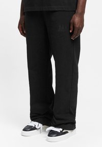 Black sweatpants with a relaxed fit, featuring a subtle logo detail on the leg and paired with black and white sneakers.