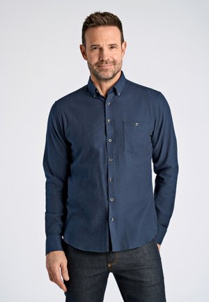Marineblaue Knopf-down-Hemd aus weichem Stoff, mit einer Brusttasche und einem Button-down-Kragen, kombiniert mit dunklen Jeans.