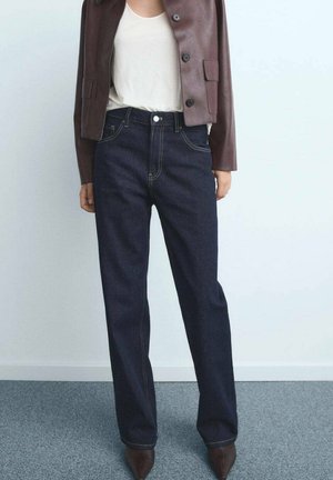 Jeans indaco scuri a vita alta con vestibilità dritta, rifiniti con cuciture a contrasto sottili. Abbinati a un giubbotto cropped in pelle marrone.